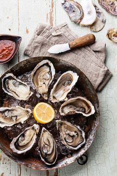 oysters in an iron skillet with lemon wedges and sauce on the side