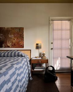 a bedroom with a bed, desk and door leading to another room that has a painting on the wall