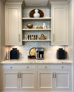 a kitchen with white cabinets and marble counter tops, along with gold accessories on the shelves