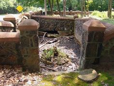 an old stone bridge with moss growing on the ground and trees in the backround