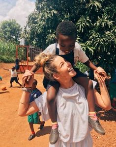 a woman is carrying a child on her shoulders while others watch from the dirt ground