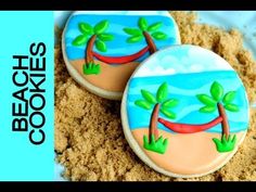 two decorated cookies sitting on top of a pile of sand next to the ocean and palm trees