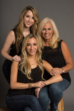 three women sitting on top of a wooden stool posing for a photo with their arms around each other