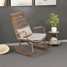 a rocking chair next to a small table with a potted plant on it in front of two paintings