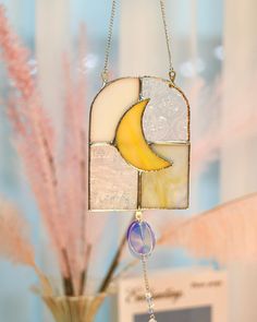 a stained glass sun catcher hanging from a chain next to a vase filled with flowers