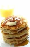 a stack of pancakes sitting on top of a white plate next to a glass of orange juice