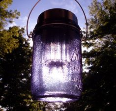 a blue mason jar hanging from a tree with the sun shining through trees in the background