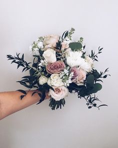 a bouquet of flowers being held by someone's hand on a white wall background