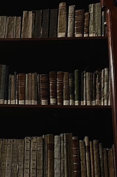 an old bookshelf filled with lots of books in a dark room next to a clock