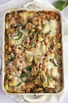 a casserole dish filled with meat, cheese and spinach sprinkled with basil