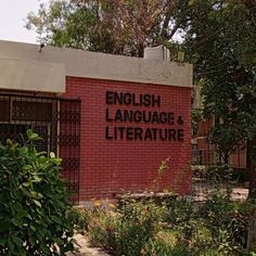 an english language and literature sign in front of a red brick building surrounded by greenery