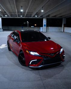 a red car is parked in an empty parking garage with no one around it at night