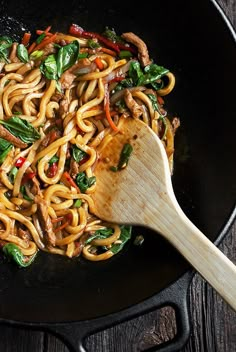 a wok with noodles and vegetables cooking in it on top of a wooden table