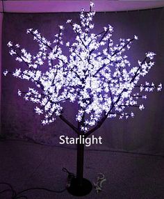 a lighted tree in the middle of a room with purple lights on it and a white background