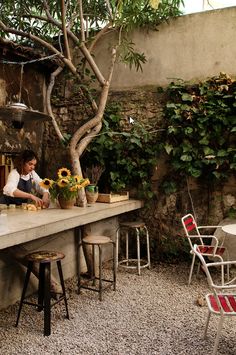 a woman sitting at a bar with sunflowers on the counter and chairs around it