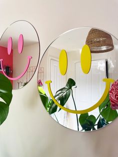 two mirrors with smiley faces on them are hanging from the wall next to a pink rose