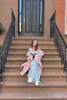 a woman is sitting on the steps in front of a door wearing a pink coat