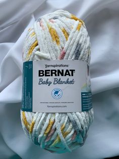 a ball of yarn that is white and yellow with some stripes on it, sitting on a bed sheet