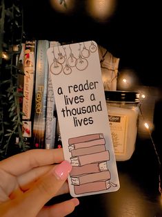 a hand holding up a bookmark that says, a reader lives a thousand lives