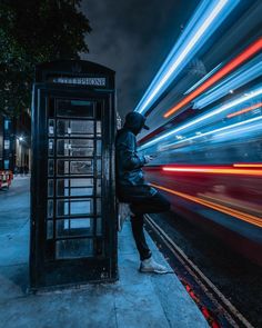 a man sitting on a telephone booth next to a street with lights in the background