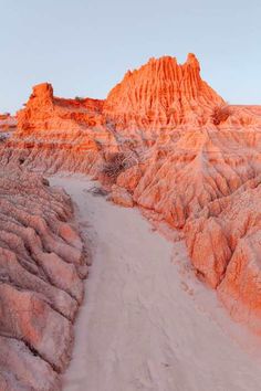 a dirt road in the middle of a desert with orange colored rocks on both sides