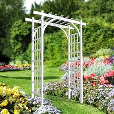 a garden with many flowers and plants around it in the day time, there is a white trellis on the grass