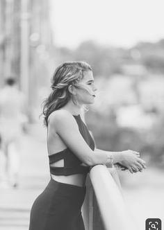 a woman leaning on a rail with her hand on her hip and looking off into the distance