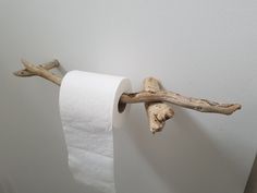 a white toilet paper roll sitting on top of a wooden branch next to a wall