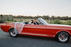 a bride and groom in an orange convertible car