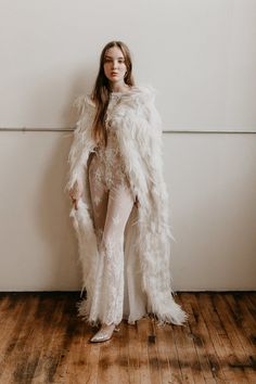 a woman standing in front of a wall wearing a white fur coat and leggings