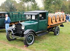 an old green truck parked on top of a lush green field next to people standing around