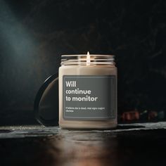 a candle sitting on top of a wooden table next to a black mug with the words will continue to monitor