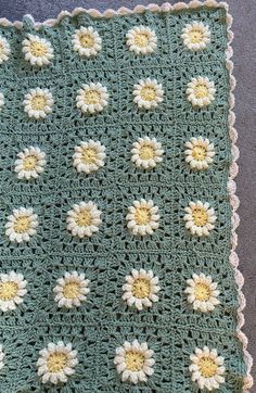 a green crocheted blanket with white and yellow flowers on it sitting on a floor