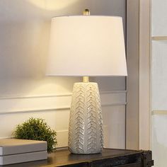 a white lamp sitting on top of a wooden table next to a book and plant