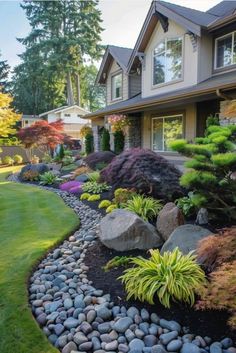 a garden with rocks and plants in front of a large house on the side of a road