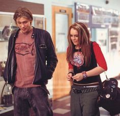 a man and woman standing next to each other looking at something on the ground in front of them