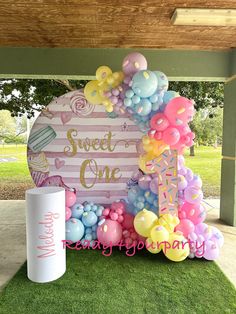 a sign that says sweet one on it and balloons in the grass next to it