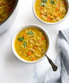 two bowls of chicken and vegetable soup on a white surface with a blue towel next to it