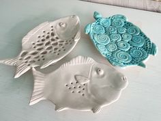 three ceramic fish sitting on top of a white table next to each other and one is blue