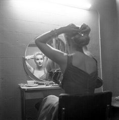 a woman sitting in front of a mirror brushing her hair