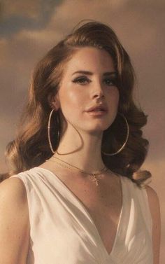 a woman wearing large hoop earrings and a white dress is standing in front of a cloudy sky