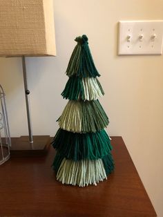 a green and white christmas tree sitting on top of a wooden table next to a lamp