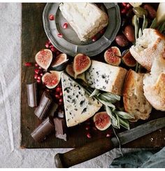 a wooden cutting board topped with lots of different types of cheeses and fruit on top of it