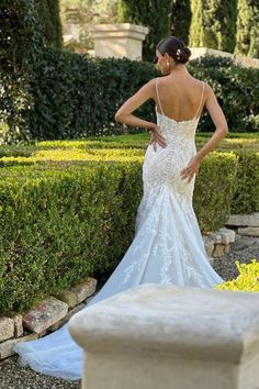 a woman in a white wedding dress standing next to a stone bench and shrubbery