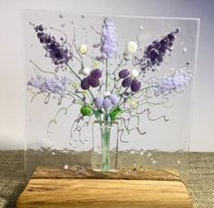 a vase filled with purple flowers sitting on top of a wooden block