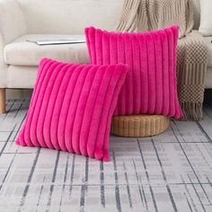 two pink pillows sitting next to each other on top of a rug in front of a white couch