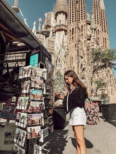 a woman standing next to a book stand in front of a tall building with spires