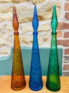 three colorful vases sitting on top of a wooden table next to a brick wall