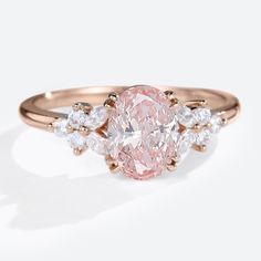 a pink diamond ring with white diamonds on the band and an oval shaped center stone