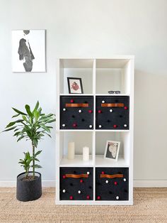 a white bookcase with black and red bins next to a potted plant